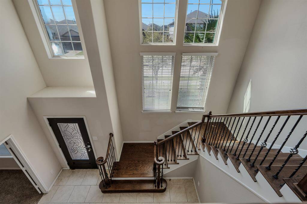 The staircase has elegant wooden steps and wrought iron railings, leading to the upper level. The entryway is tiled, and the front door includes decorative glass detailing.