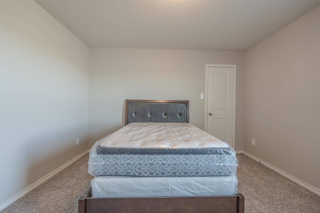 Cozy bedroom with neutral walls and carpet, featuring a bed with a tufted headboard and a door leading to additional space or storage.
