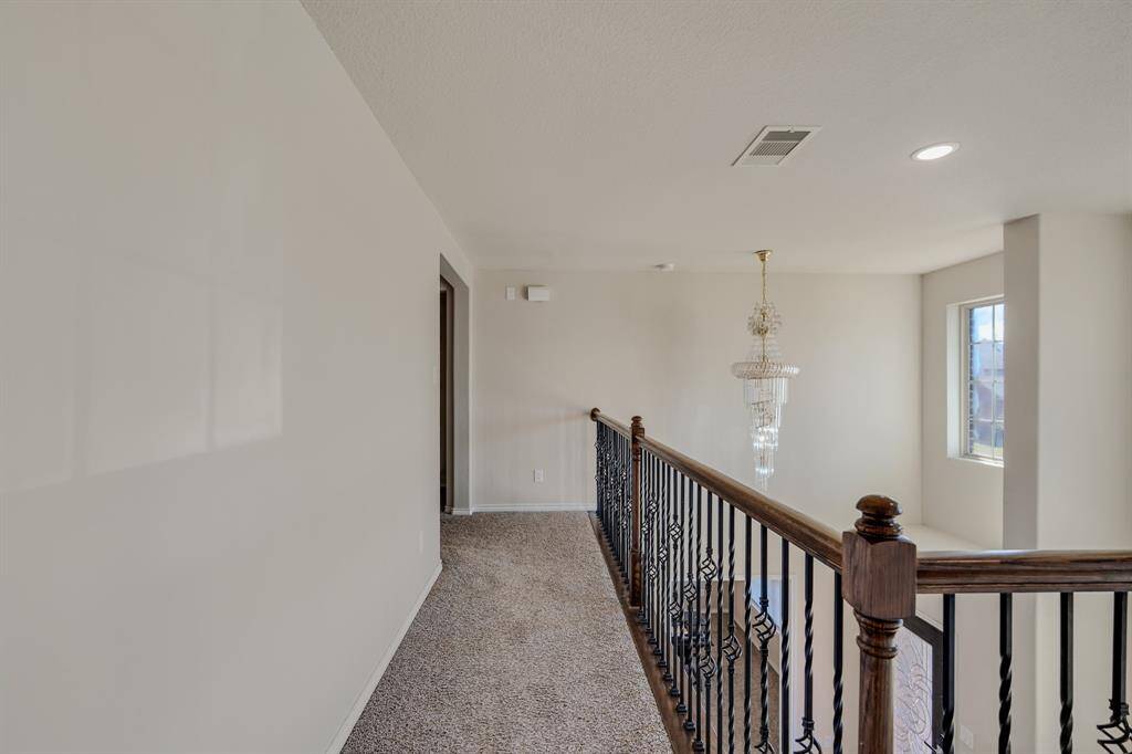 Bright upstairs hallway with carpeted floors and iron railing. A large window allows natural light, and a chandelier adds elegance.