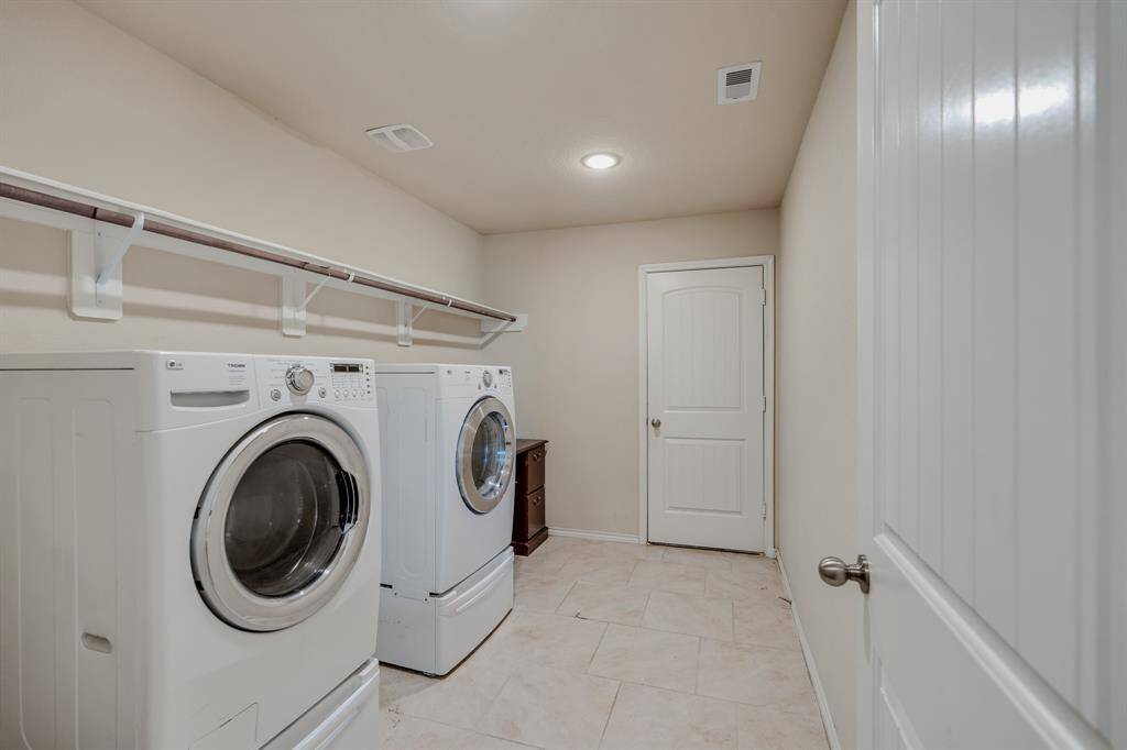 Spacious laundry room with modern washer and dryer, ample shelving for storage, and neutral tile flooring.