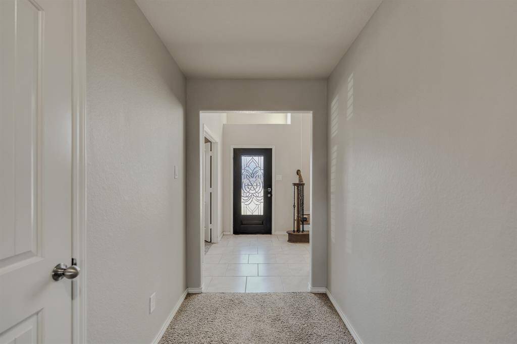 Bright and inviting entryway featuring neutral walls, carpeted hallway, and a stylish glass front door with intricate design. Natural light enhances the space, leading into a tiled area and showcasing a staircase.