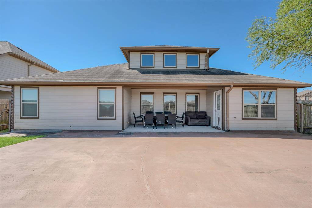 There is outdoor seating, and the exterior features several windows, providing ample natural light. The yard is partially paved and includes some green space.
