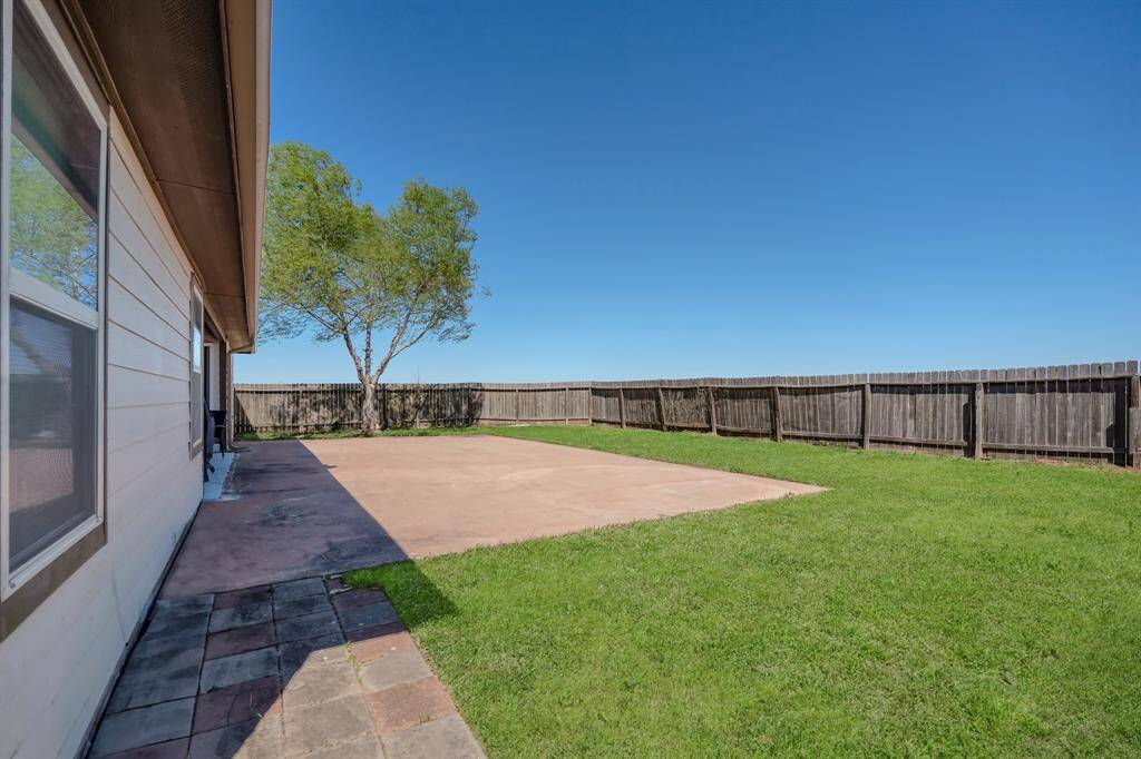 This backyard features a spacious fenced area with a concrete patio, grassy lawn, and a couple of trees, ideal for outdoor activities and relaxation.