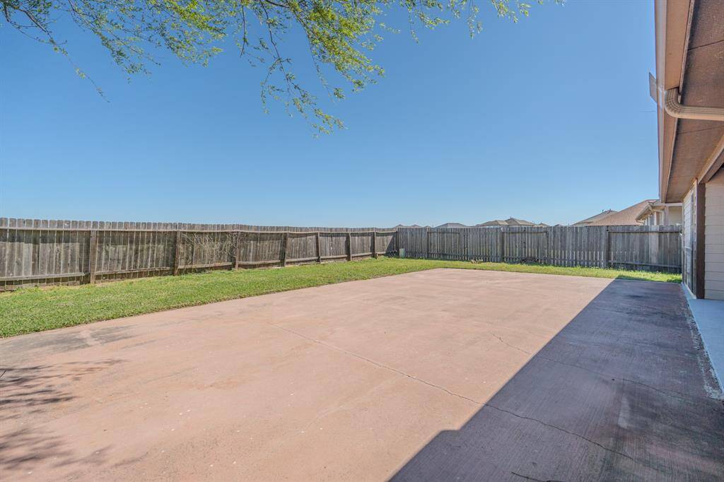 This backyard features a spacious concrete patio, ideal for outdoor activities, surrounded by a wooden fence for privacy. There's a small strip of grass along the fence, offering a touch of greenery.