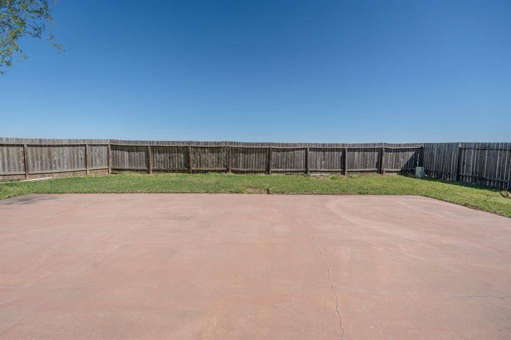 Spacious backyard with a large concrete patio, perfect for outdoor activities. Surrounded by a wooden fence for privacy and a small grassy area for greenery.