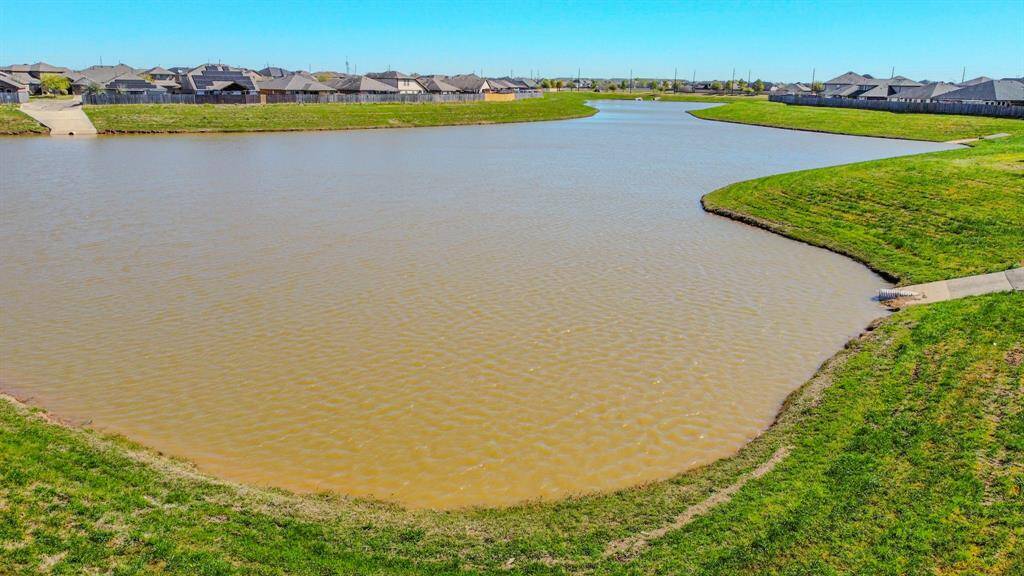 Neighborhood pond, bordered by gently sloping grassy banks, with houses in the background. Ideal for buyers seeking a tranquil setting.