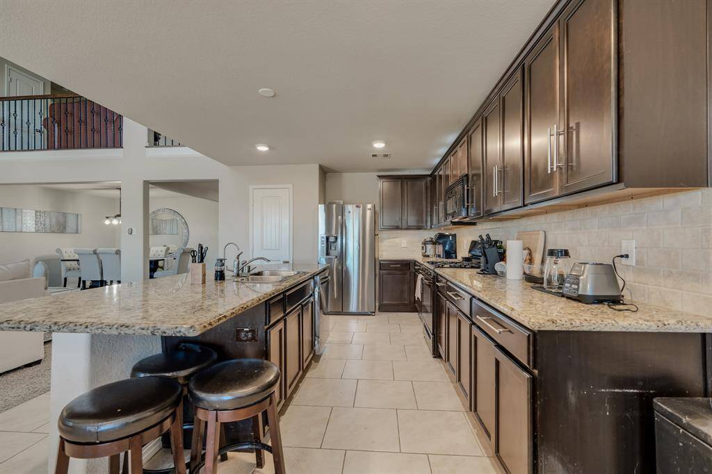 Modern kitchen featuring dark wood cabinets, granite countertops, and stainless steel appliances. The open layout connects to a dining area, enhancing the home's flow and functionality.