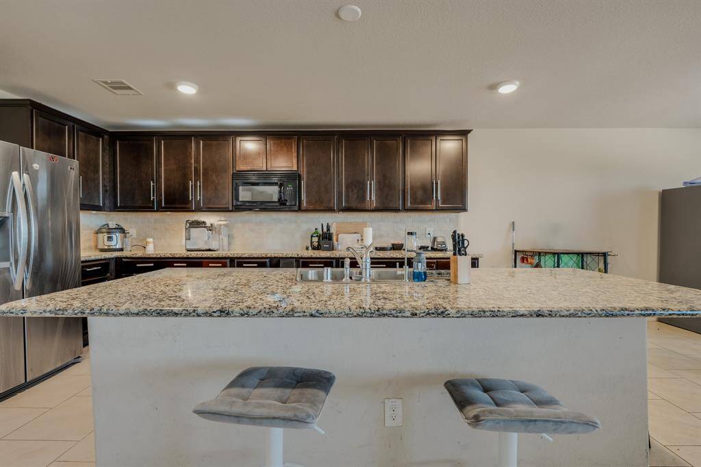 This kitchen features dark wood cabinets, granite countertops, a large island with seating, stainless steel appliances, and ample lighting, creating a modern and functional space.