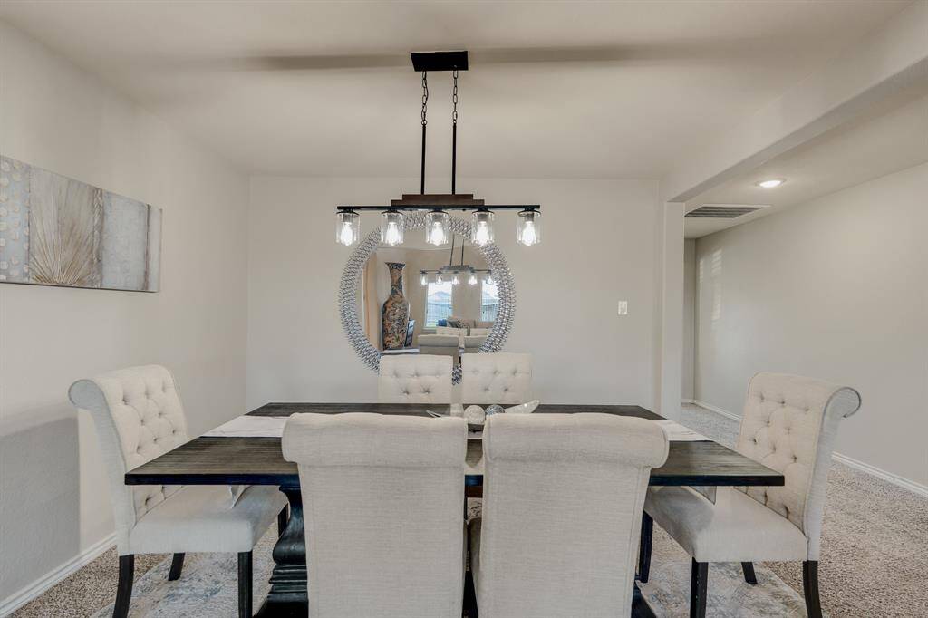 This dining room features a modern chandelier above a dark wood table surrounded by elegant, upholstered chairs. The neutral walls complement a stylish round mirror and decorative artwork, creating a cozy and inviting atmosphere.
