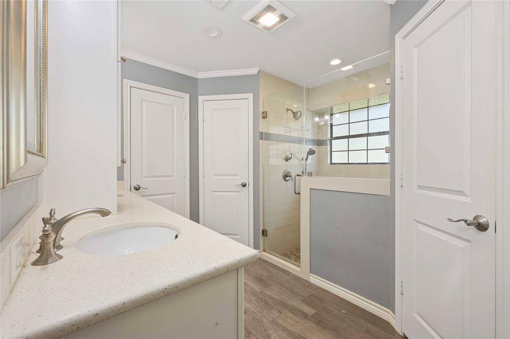 This bathroom features a modern design with a glass-enclosed shower, sleek fixtures, and ample natural light. The neutral color palette and wood-style flooring create a clean and inviting space.