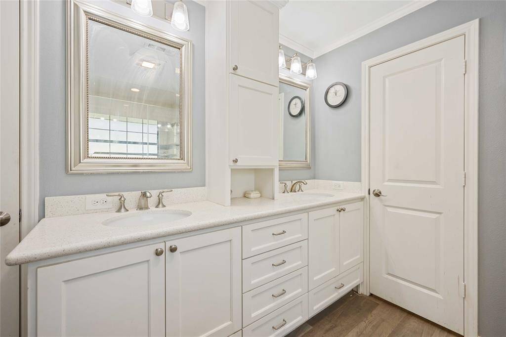 This bathroom features a sleek double vanity with ample storage, modern fixtures, and elegant mirrors. The space is bright and well-lit, with a clean, neutral color palette and a stylish wooden floor.