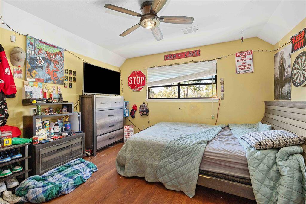 Cozy bedroom with a vaulted ceiling and ceiling fan, featuring warm yellow walls. The room includes a large window for natural light.