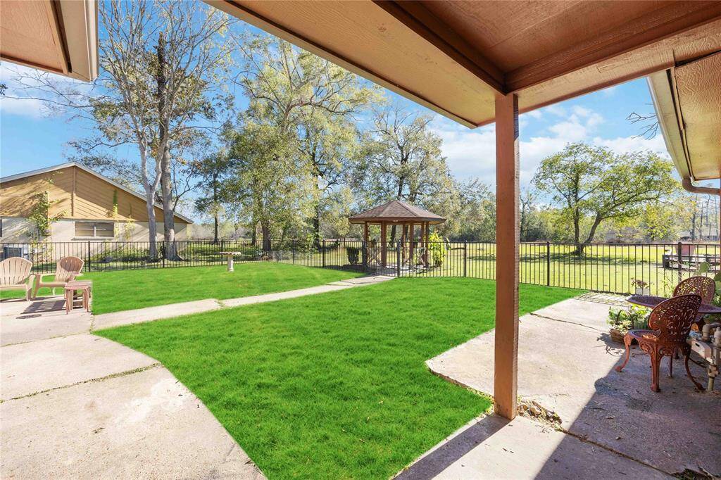 This photo showcases a spacious backyard with lush green grass, a charming gazebo, and a paved patio area. The yard is enclosed with a fence, offering privacy and a peaceful view of mature trees, perfect for outdoor relaxation or entertaining.