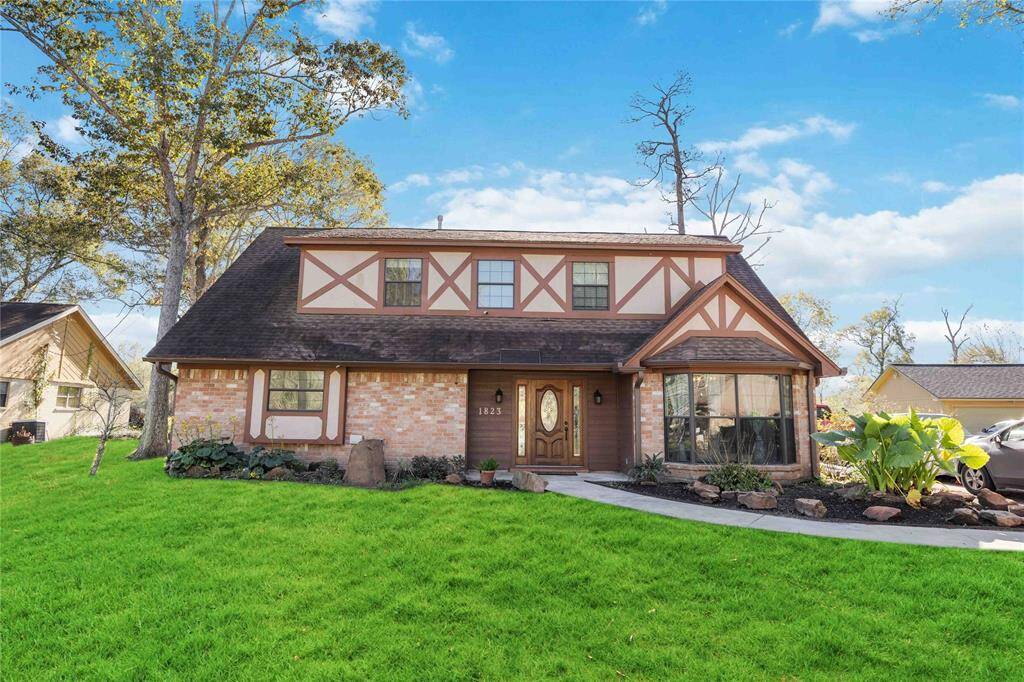 Charming two-story Tudor-style home with a brick and wood facade, featuring a manicured lawn and mature trees. A welcoming pathway leads to an elegant front door, complemented by large bay windows. Ideal for those seeking character and curb appeal.