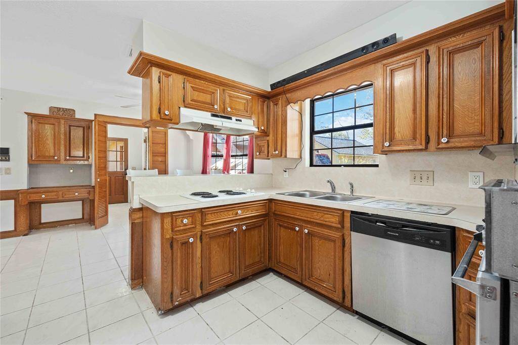 This kitchen features warm wooden cabinetry, a double sink, and modern stainless steel appliances. It offers a cozy layout with ample natural light from the large window, and a convenient pass-through to the adjoining room.