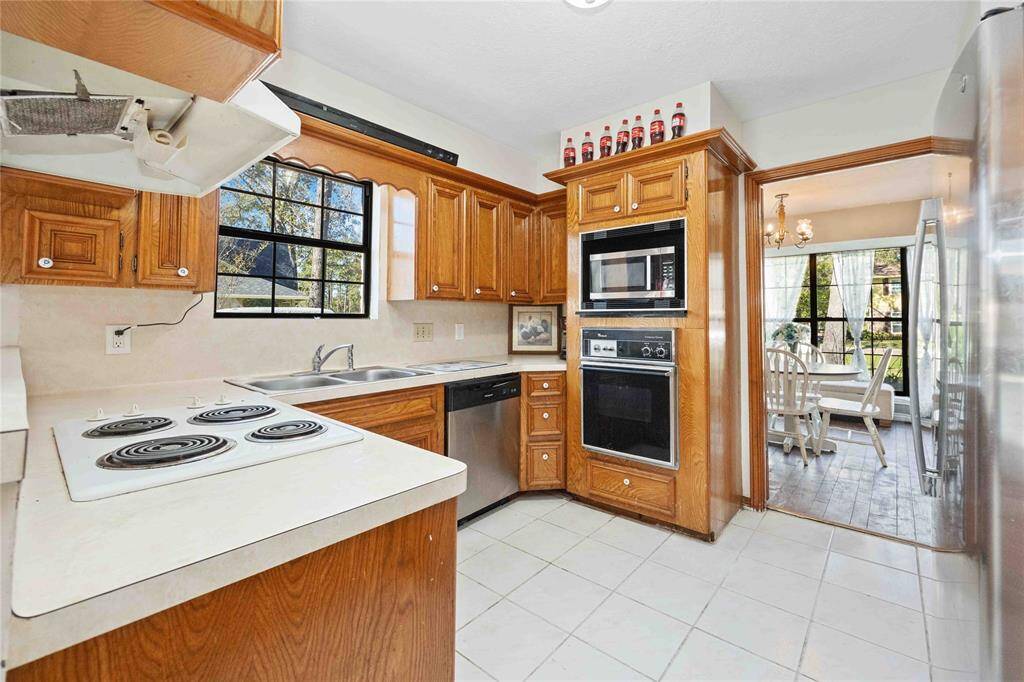 This kitchen features wood cabinetry, a built-in oven, and a stovetop. It opens to a bright dining area with large windows, providing a cozy and functional space for cooking and family meals.