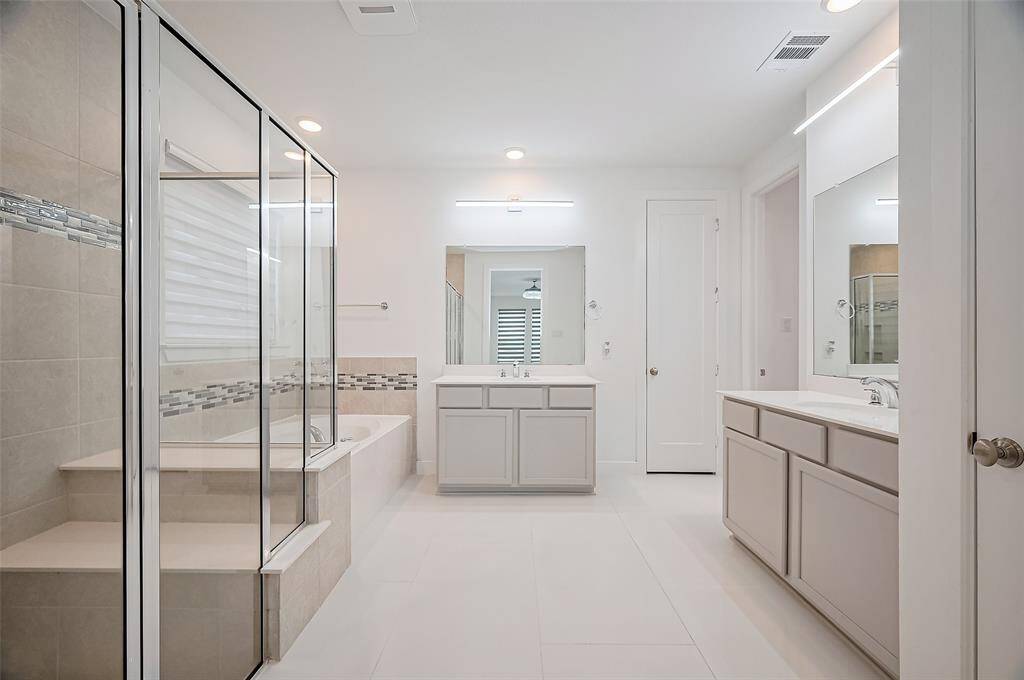 A spa-like haven featuring a glass-enclosed shower with built-in bench, a deep soaking tub, and two beautifully illuminated vanities. Elegant cabinetry below offers plenty of storage, combining luxury with everyday practicality.