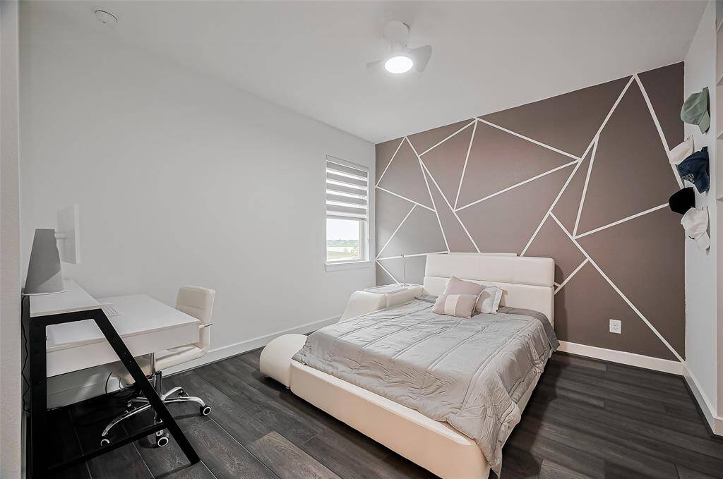 A bold accent wall adds personality to this stylish bedroom, complemented by rich dark-toned flooring and ample space for comfort and creativity.