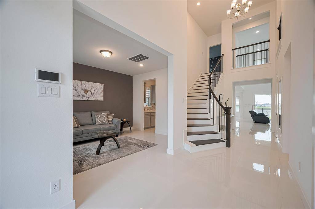Step through the front doors into a sophisticated space where the formal living area is perfectly framed by a broad interior doorway. A graceful staircase draws the eye upward toward the soaring ceiling and chandelier, while glimpses of the main living area hint at the spaciousness beyond.
