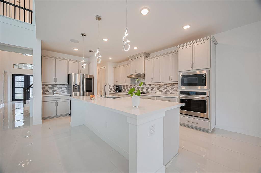 The kitchen is both impressive and functional, anchored by a massive island beneath a trio of pendant lights. Stylish cabinetry and an eye-catching backsplash add flair, while the layout invites easy connection to the nearby dining area.