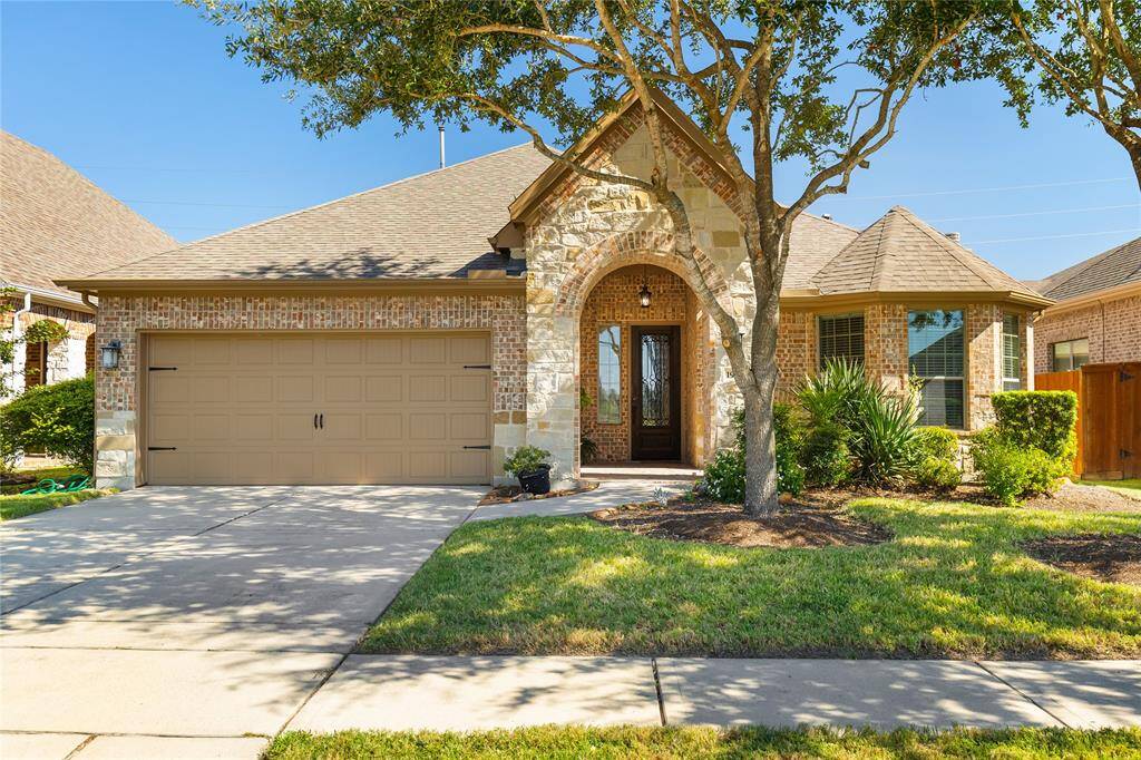 This home features a charming brick exterior with a two-car garage and a welcoming arched entryway. The front yard is landscaped with mature trees and shrubs, providing a pleasant curb appeal.