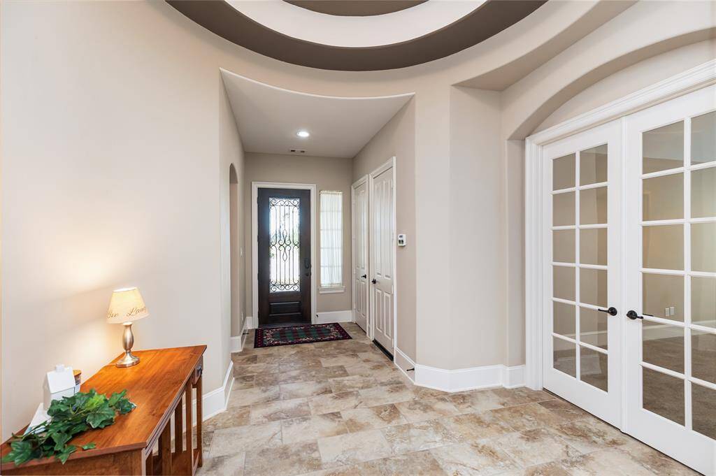 This photo showcases a bright, welcoming entryway with a stylish front door, elegant tile flooring, and French doors leading to an office or game room.