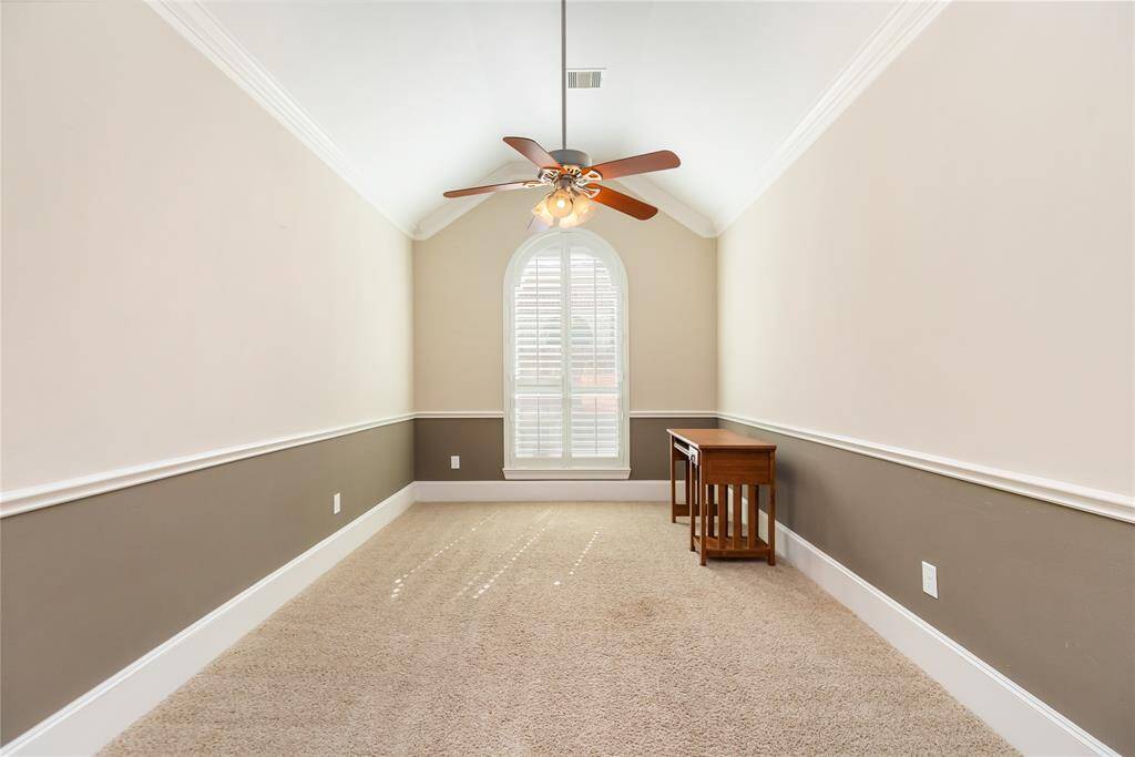 Game room or office space with neutral walls and a vaulted ceiling. It features a ceiling fan with lights and a large arched window with shutters, offering natural light.