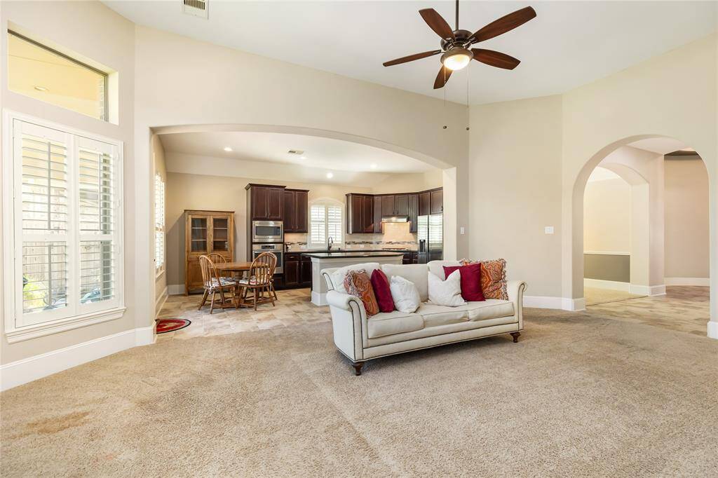 This spacious living area features an open floor plan with a cozy sofa, ceiling fan, and access to the kitchen and dining space. The kitchen boasts dark wood cabinets, and built-in oven. Arched doorways and ample natural light enhance the inviting atmosphere.