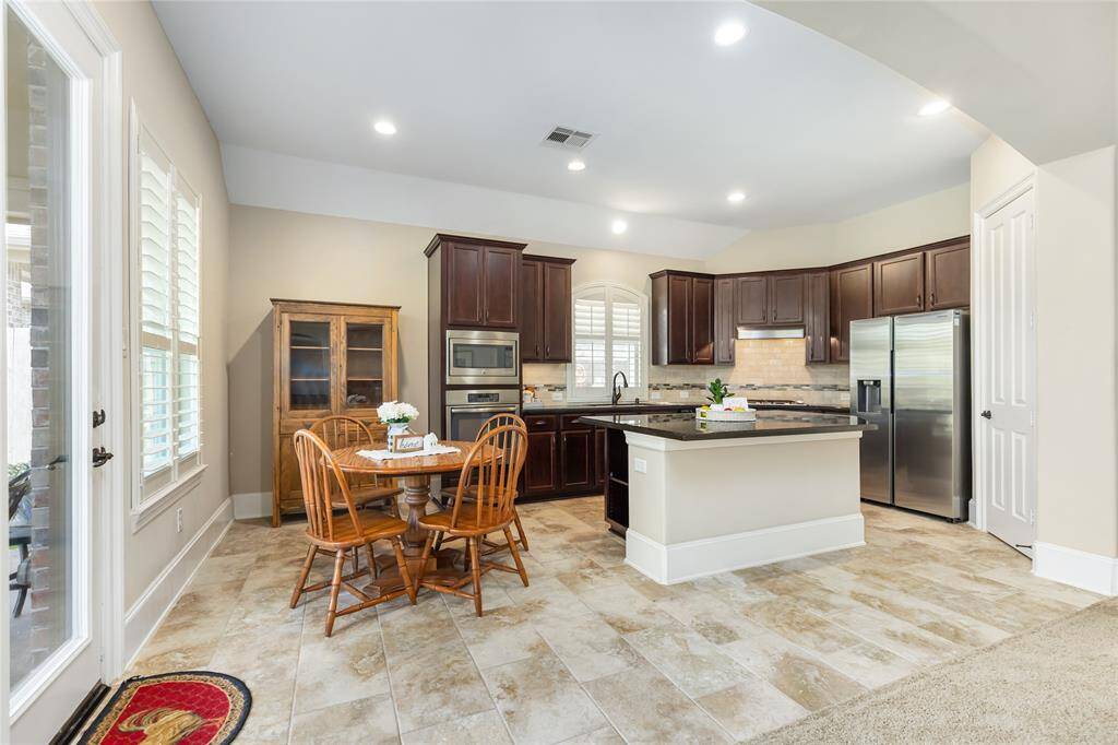 This spacious kitchen features dark wood cabinets, stainless steel appliances, and a large island with granite countertops. It includes a cozy dining nook with natural light from large windows and tile flooring for easy maintenance.