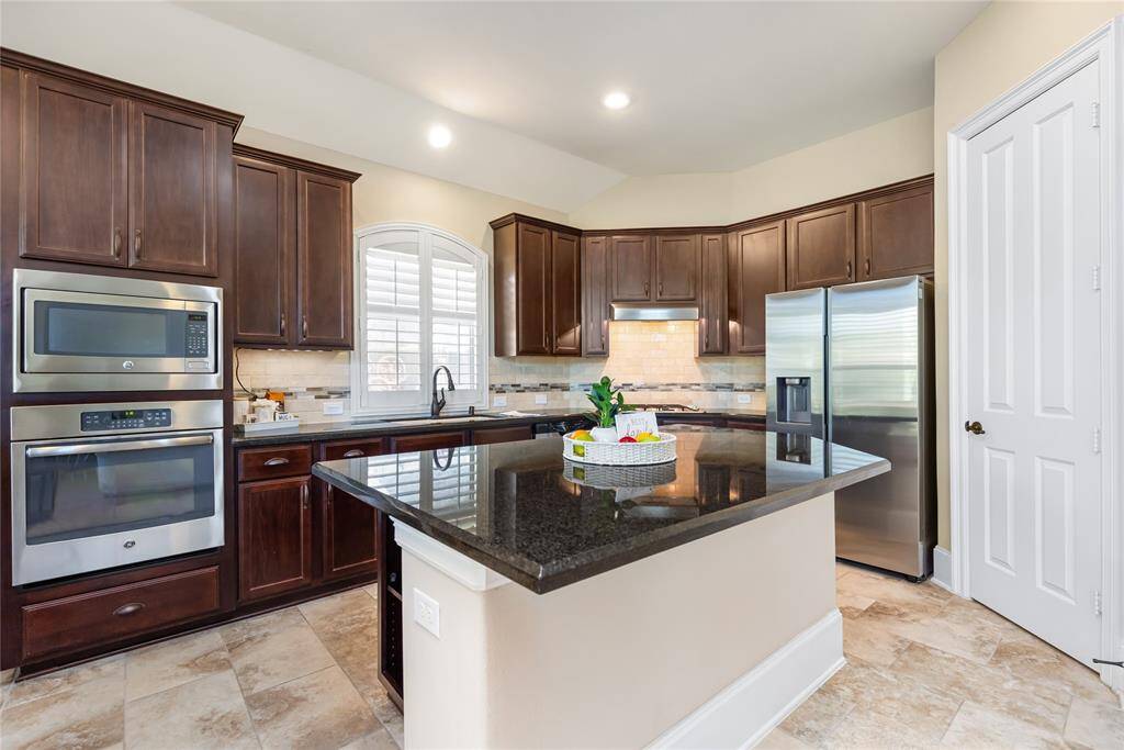 This kitchen features elegant dark wood cabinets, stainless steel appliances, and a spacious island with a sleek black countertop. The room is well-lit with recessed lighting and has a large window above the sink, providing a bright and inviting atmosphere.