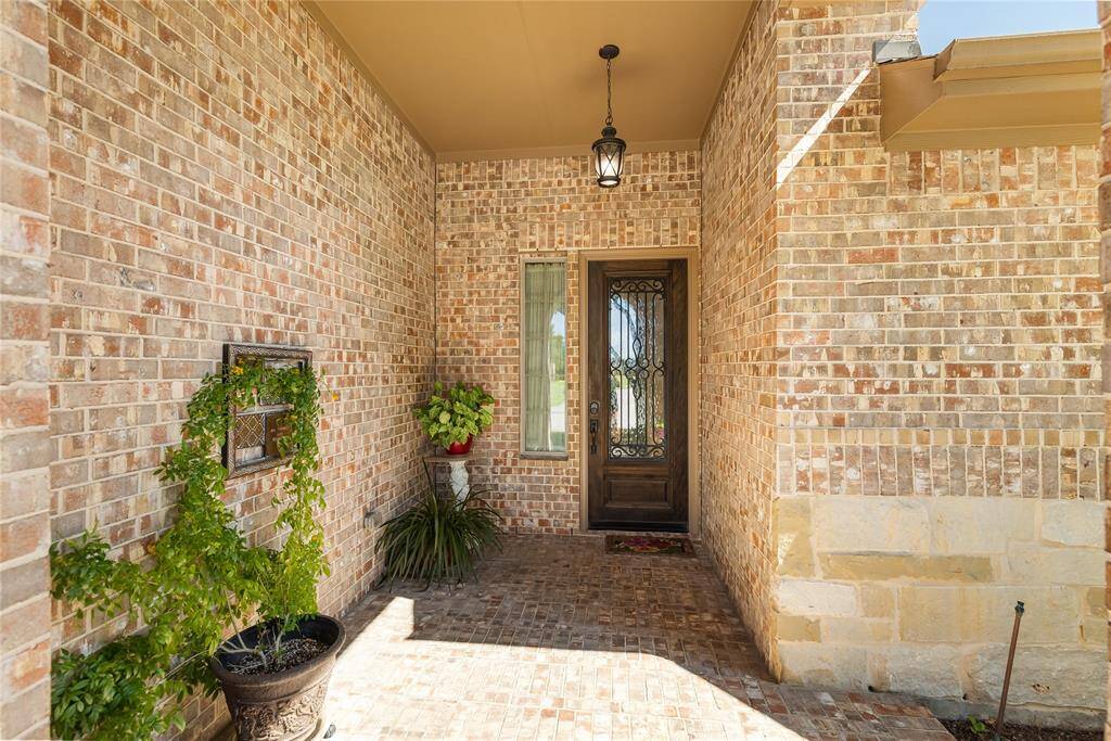 Charming brick entryway with a front door with a decorative wrought iron over the glass and elegant lantern lighting.