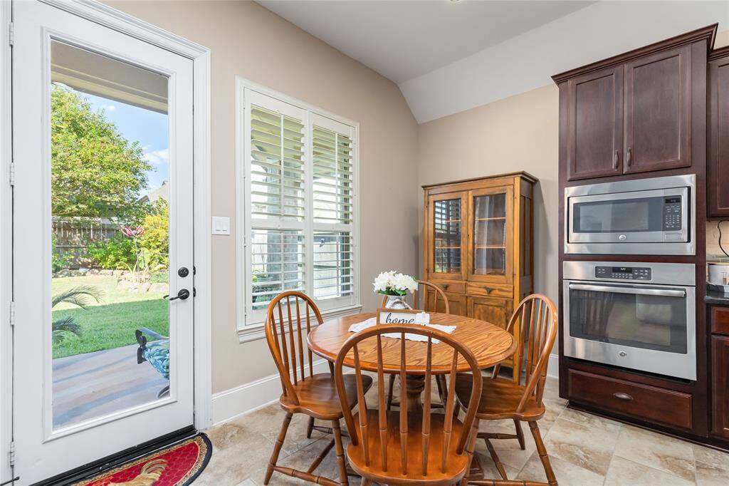 This bright dining area features a glass door, that opens to a lush backyard and large windows allowing natural light. Modern appliances are built into the dark wood cabinetry.