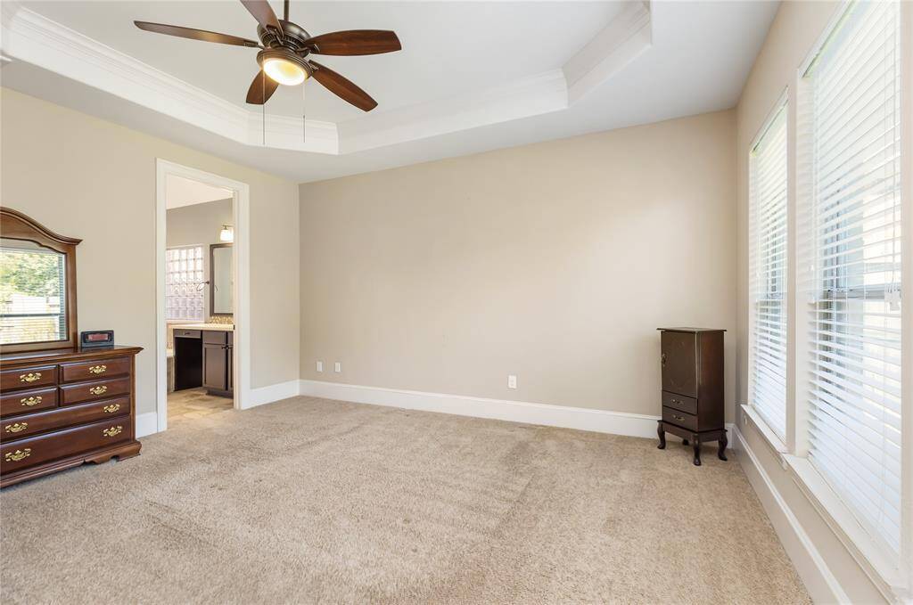 This spacious Primary bedroom features neutral walls, a ceiling fan, and plenty of natural light from large windows. It includes carpeted floor and you can see the primary bath.