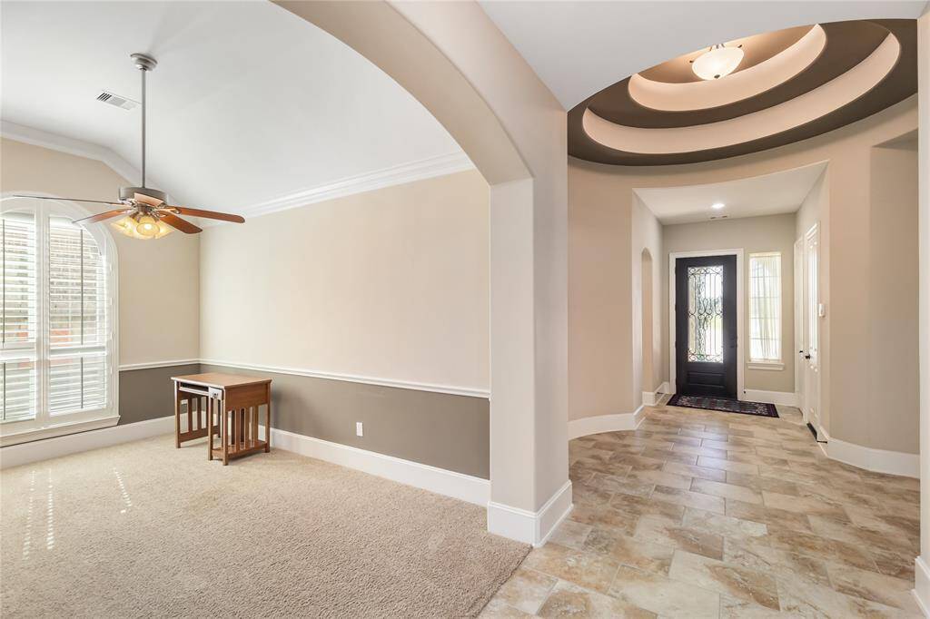 This photo showcases a bright entryway with tiled flooring, elegant ceiling design, and a welcoming front door. Adjacent could be perfect for a cozy living area or home office, with a large arched window and ceiling fan.