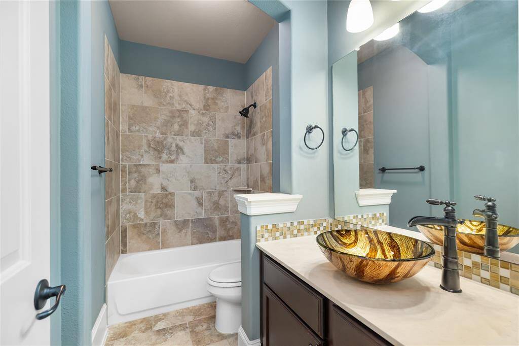 This bathroom is off the hallway leading to the front bedrooms, features a stylish vessel sink with a unique design, modern fixtures, and a tiled shower-tub combo. The walls are painted in a soothing teal tone, complemented by a large mirror and ample lighting.