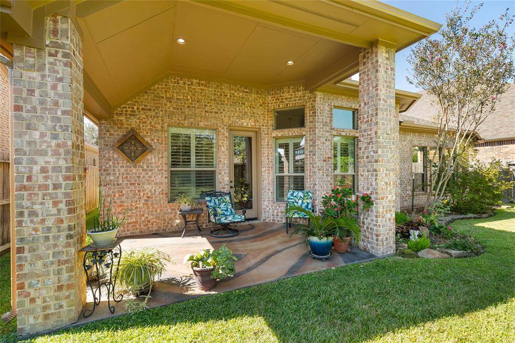 This photo showcases a charming covered patio with brickwork and cozy seating, surrounded by lush greenery and potted plants, offering a serene outdoor space for relaxation.