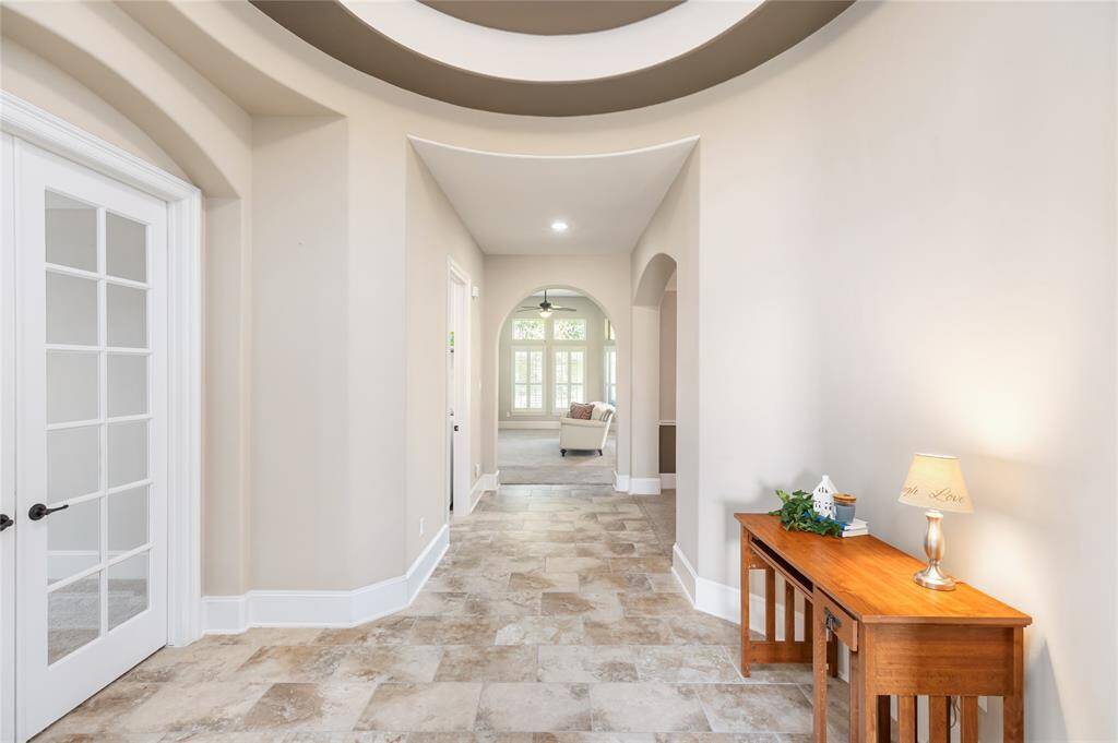 This welcoming entryway features elegant tile flooring and soft neutral walls, leading to a bright living area with arched doorways.
