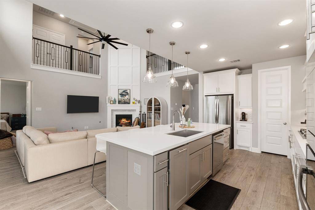 Enjoy seamless living in this stunning open layout—chef’s kitchen with island overlooks a cozy living room with fireplace, soaring ceilings, and a dramatic black ceiling fan.