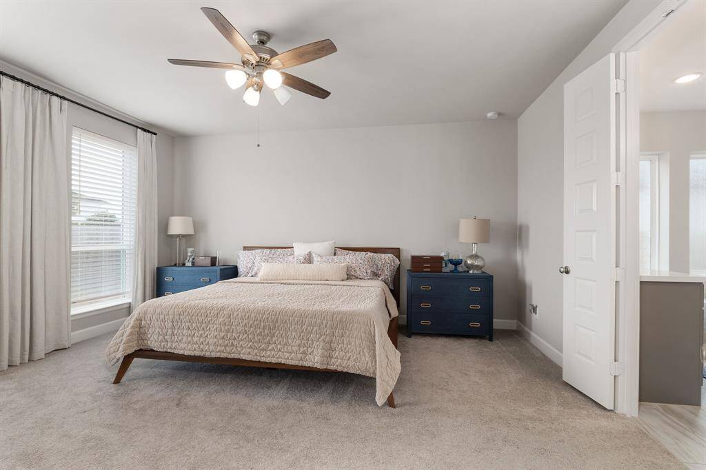 The first-floor primary retreat is a true sanctuary, designed for rest and relaxation. It features soft plush carpeting underfoot, a high ceiling with a modern ceiling fan that enhances airflow and comfort, and abundant natural light that fills the space.