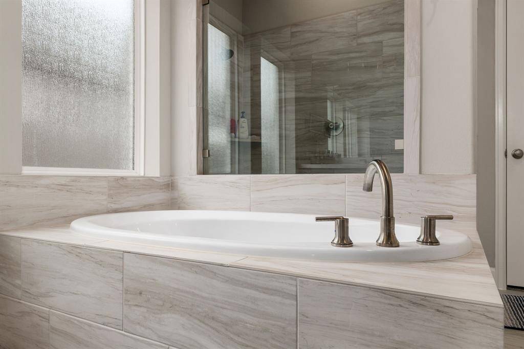 The deep soaking tub invites you to unwind after a long day, nestled beneath a large rain glass window that bathes the space in soft, natural light while maintaining complete privacy.