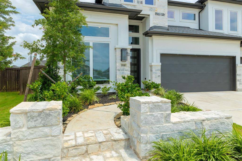 This home offers A+ curb appeal, highlighted by a paved walkway accented with a stone retaining wall and stone steps that lead to a striking exterior featuring a blend of stone, stucco & modern finishes.