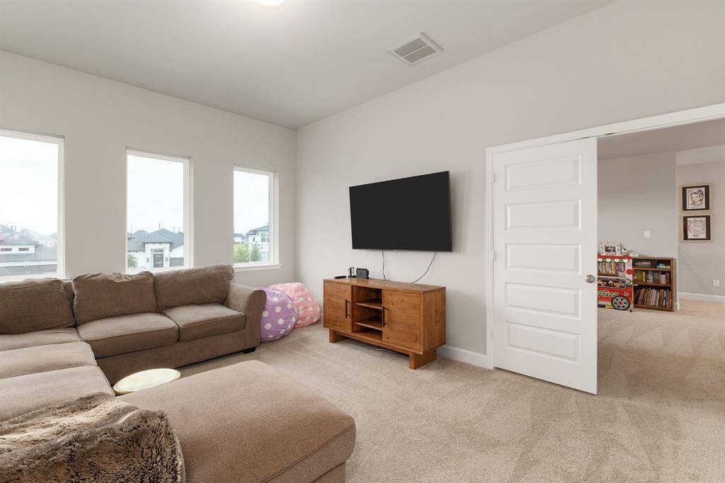 The room features plush carpeting for added comfort, a high ceiling that enhances the sense of space, and large windows that flood the area with natural light. It’s a thoughtfully designed space that balances relaxation and function.
