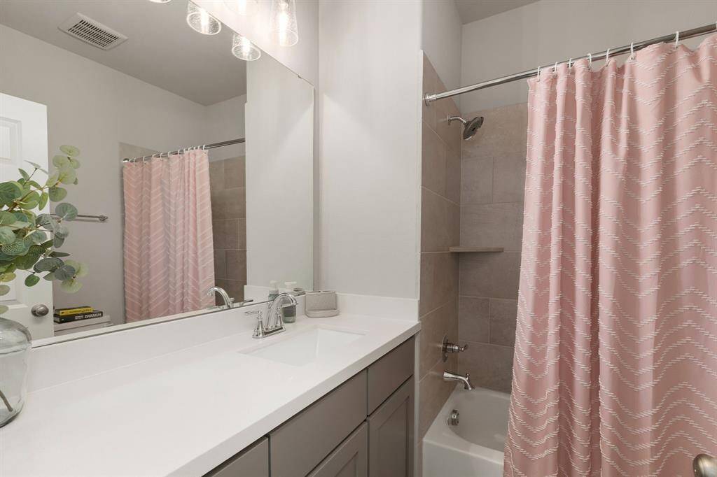 This spacious ensuite bathroom features a sleek quartz-topped vanity, elegant vanity light fixture, and a tub and shower combo—offering both style and functionality in a beautifully designed space.