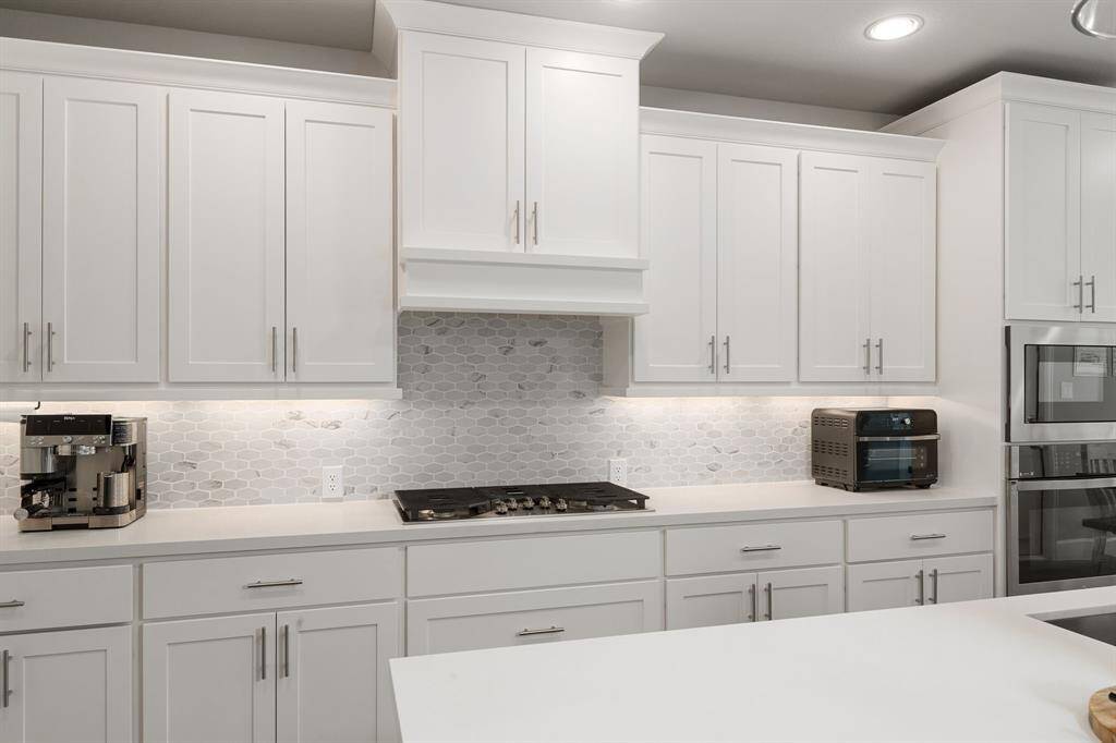Modern white shaker cabinets, a chic hex tile backsplash, and under-cabinet lighting create a stylish and functional cooking space. Includes built-in appliances and ample countertop prep area.