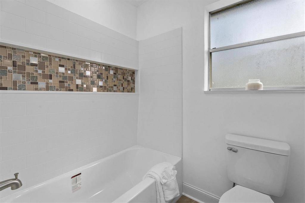 This primary full bath features hand laid tile, new tub/shower combo, and toilet!