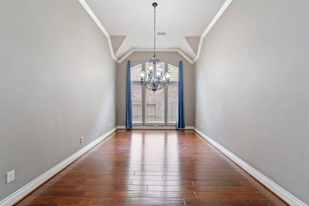 Elegant dining room with rich wood floors, crown molding, and a stylish ceiling fan.Large windows fill the space with natural light, creating a warm and inviting atmosphere.