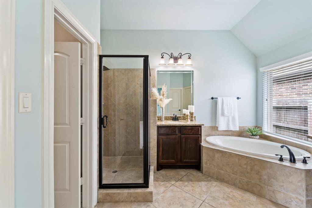 Spacious primary bathroom with tiled floors, dual vanities with lighting, and a separate tiled tub and shower.