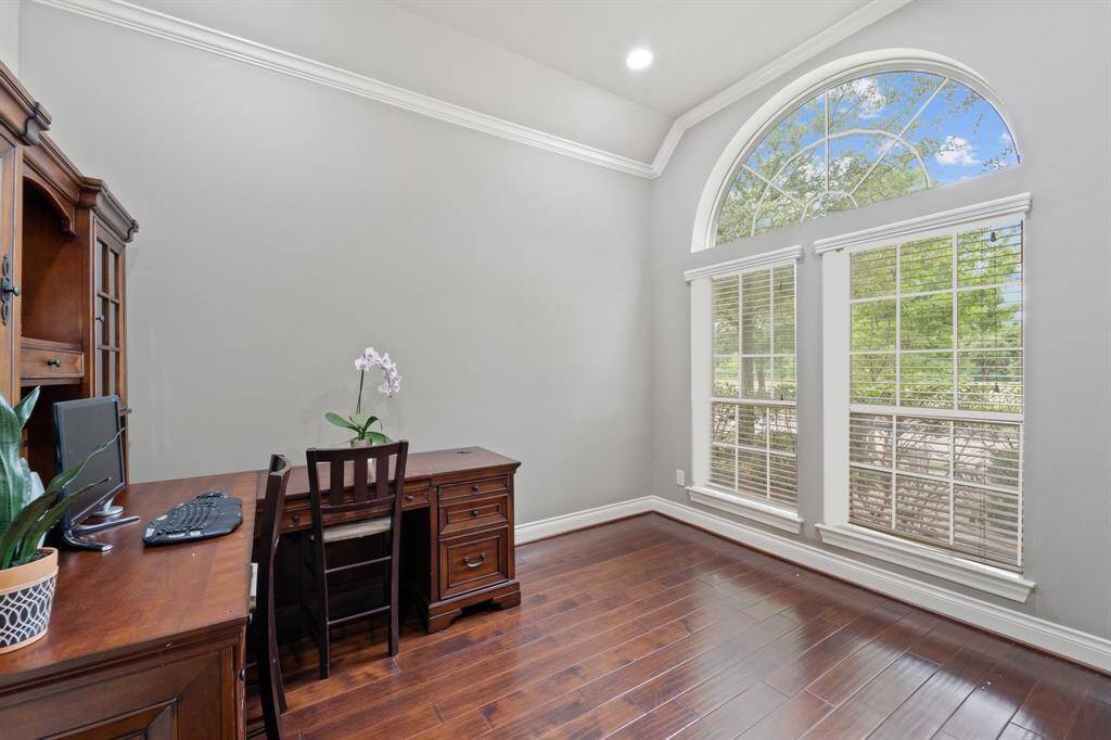 The office features warm wood floors, recessed lighting, and large windows with blinds for natural light and privacy.