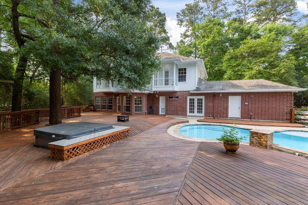 This photo showcases a spacious backyard featuring a wooden deck, a pool, and a hot tub. The two-story brick house is surrounded by lush greenery, providing a private and serene atmosphere. Perfect for outdoor entertaining and relaxation.