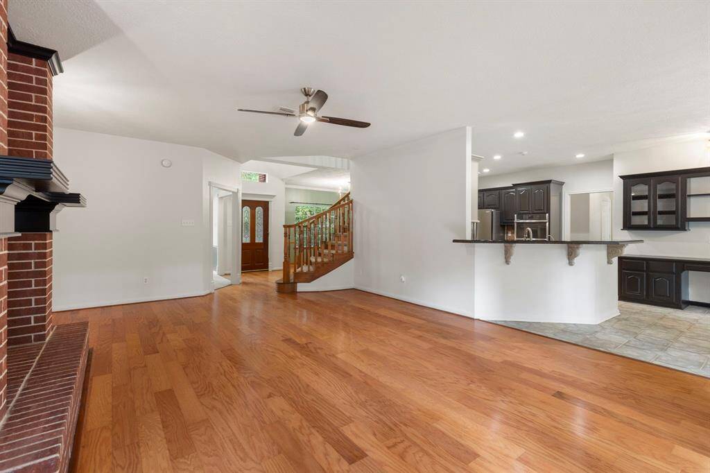 This spacious open-concept living area features hardwood floors, a brick fireplace, and a ceiling fan.